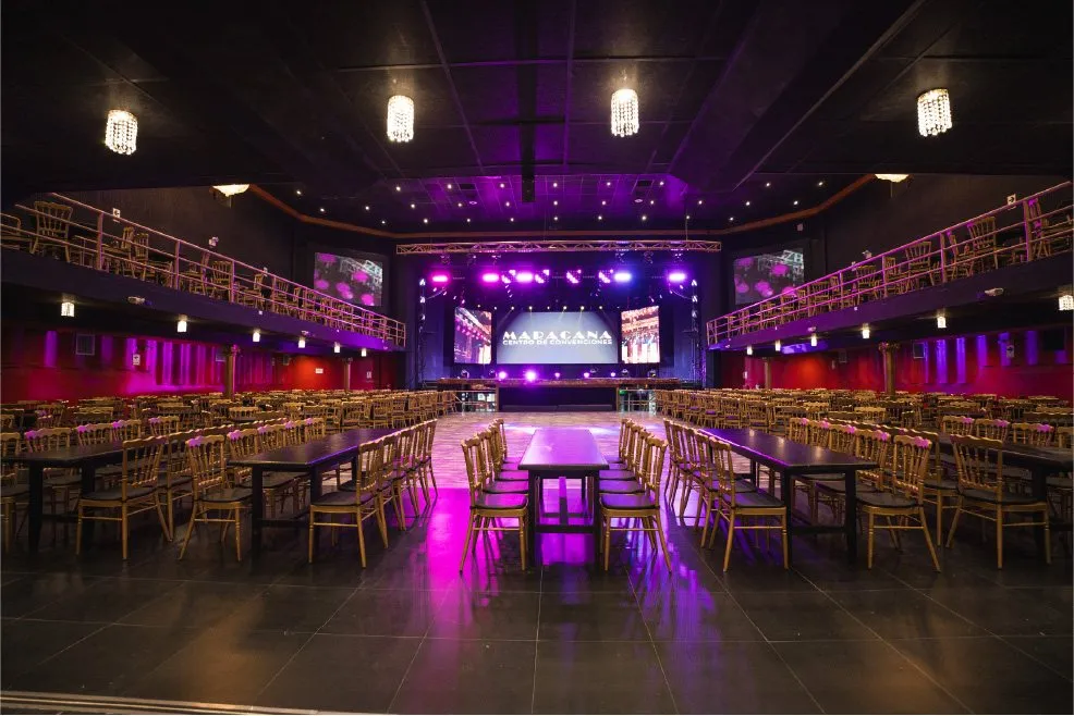 Salón de C.C. Maracaná montado con mesas y sillas doradas frente al escenario con pantalla LED